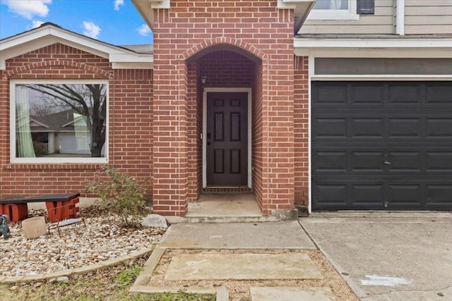 entrance to property featuring a garage, concrete driveway, and brick siding