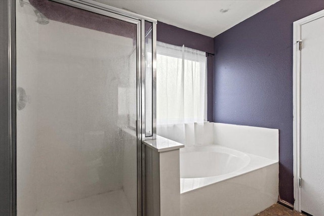 bathroom with a textured wall, a stall shower, and a garden tub