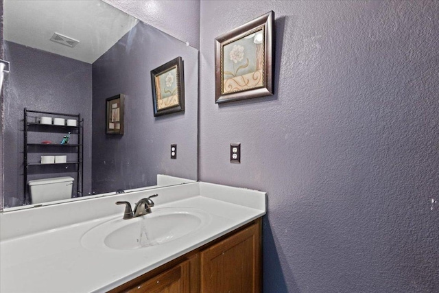 bathroom featuring visible vents, a textured wall, vanity, and toilet