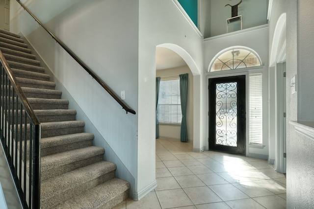 entrance foyer with a towering ceiling, light tile patterned floors, stairs, and a wealth of natural light