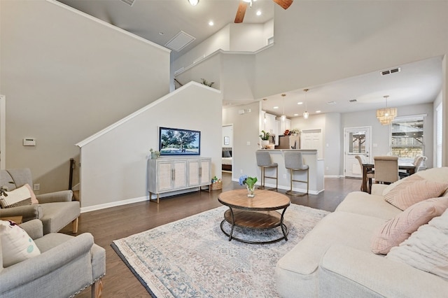 living area featuring baseboards, visible vents, dark wood finished floors, a high ceiling, and ceiling fan with notable chandelier