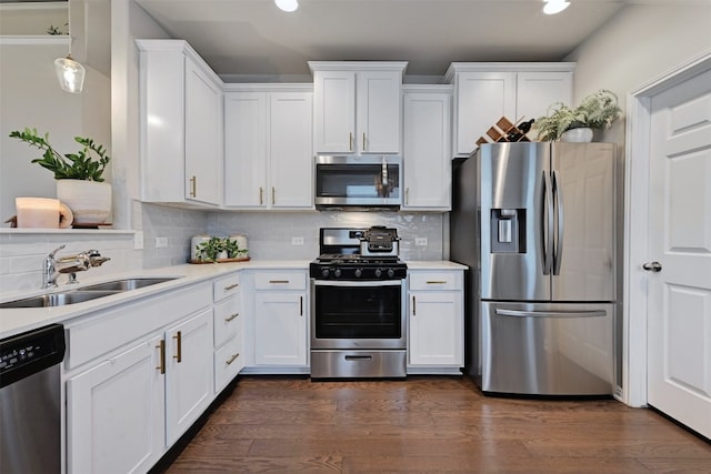 kitchen with white cabinets, dark wood finished floors, appliances with stainless steel finishes, light countertops, and a sink