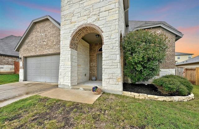 exterior entry at dusk with fence, concrete driveway, and brick siding