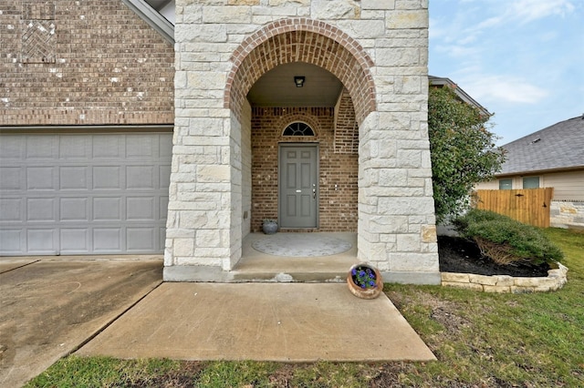 property entrance featuring stone siding, brick siding, an attached garage, and fence