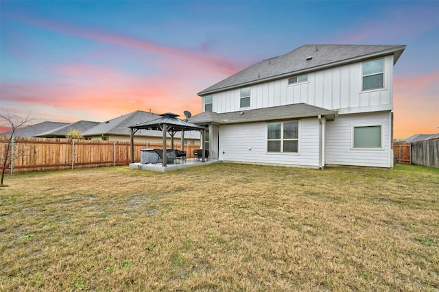 back of property at dusk with a lawn, a patio, a fenced backyard, a gazebo, and board and batten siding