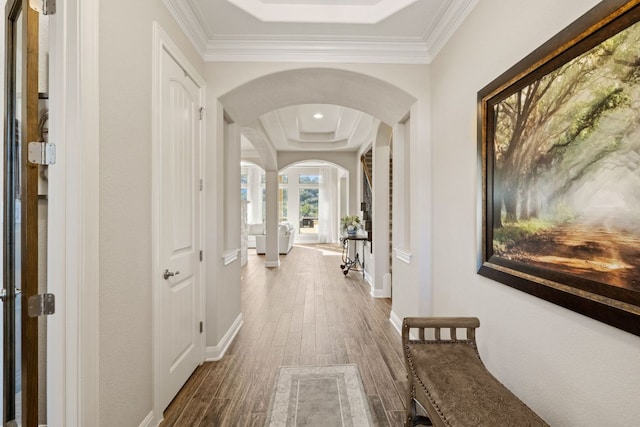 corridor featuring arched walkways, wood finished floors, a raised ceiling, and baseboards