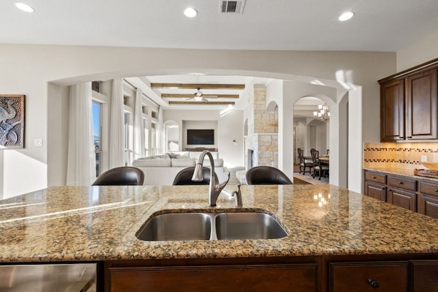 kitchen with ceiling fan, a sink, visible vents, dark stone counters, and tasteful backsplash