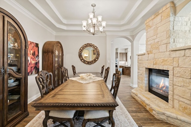 dining room with a tray ceiling, dark wood-style flooring, a fireplace, and an inviting chandelier