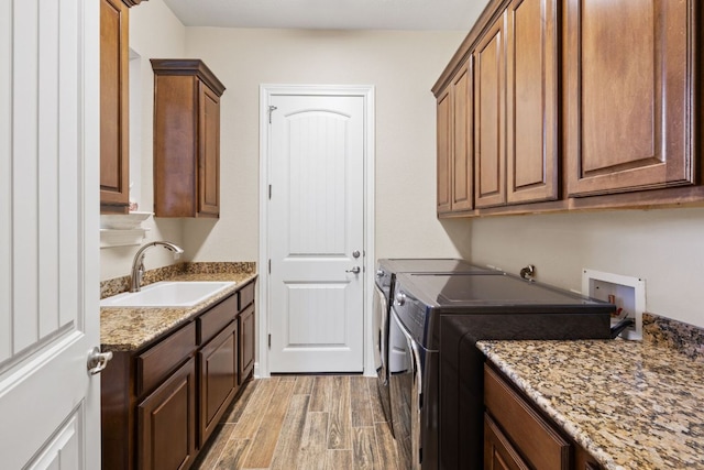 clothes washing area with light wood-type flooring, cabinet space, a sink, and independent washer and dryer