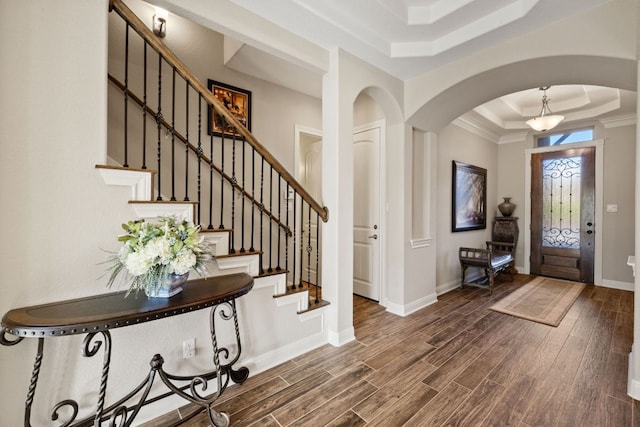 entryway with arched walkways, wood finished floors, a raised ceiling, and baseboards