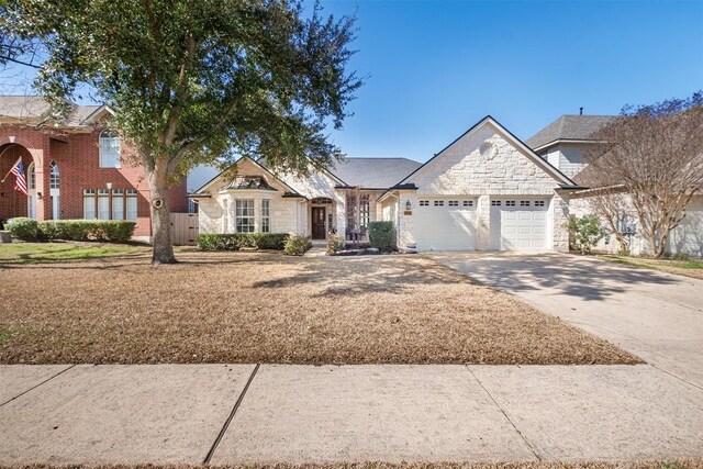 french provincial home featuring a front lawn, an attached garage, stone siding, and driveway