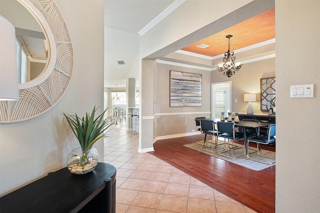 entrance foyer with light tile patterned floors, baseboards, a tray ceiling, ornamental molding, and a chandelier