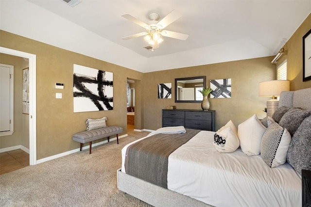 bedroom with a ceiling fan, baseboards, a tray ceiling, ensuite bath, and light colored carpet