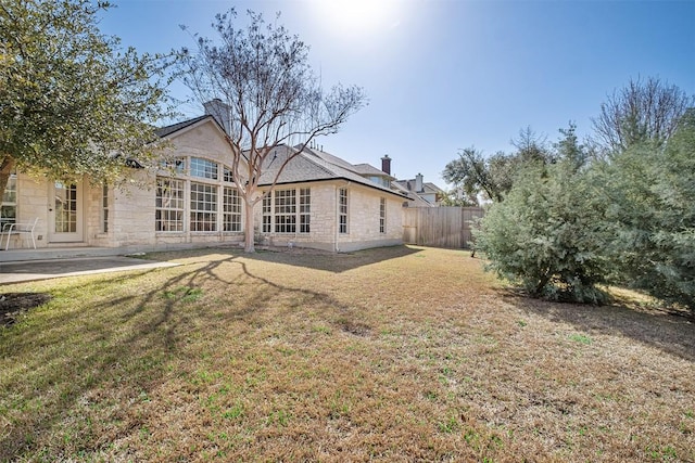 back of house featuring fence, a chimney, a yard, a patio area, and stone siding