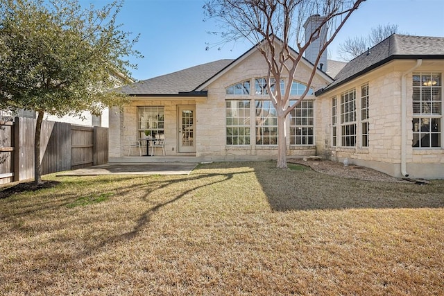 back of house featuring stone siding, a patio, a yard, and fence