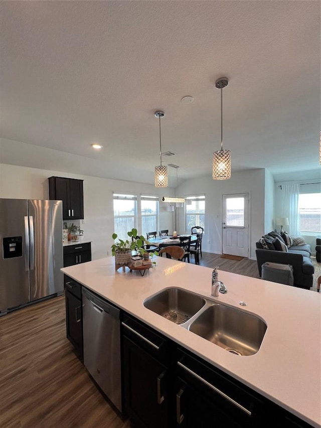 kitchen featuring a sink, open floor plan, light countertops, appliances with stainless steel finishes, and dark cabinetry