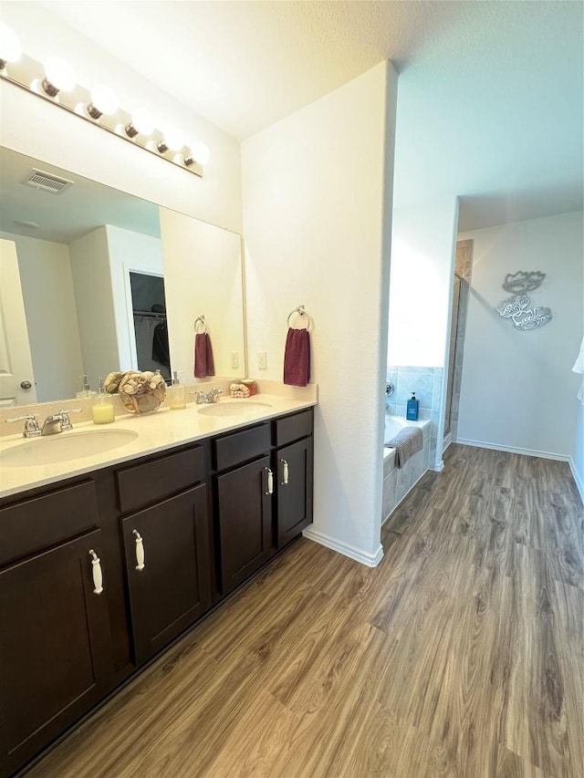 full bathroom featuring double vanity, a garden tub, a sink, and wood finished floors