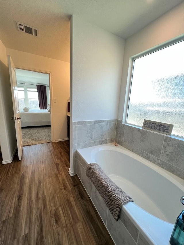 full bath featuring ensuite bathroom, wood finished floors, visible vents, and a bath