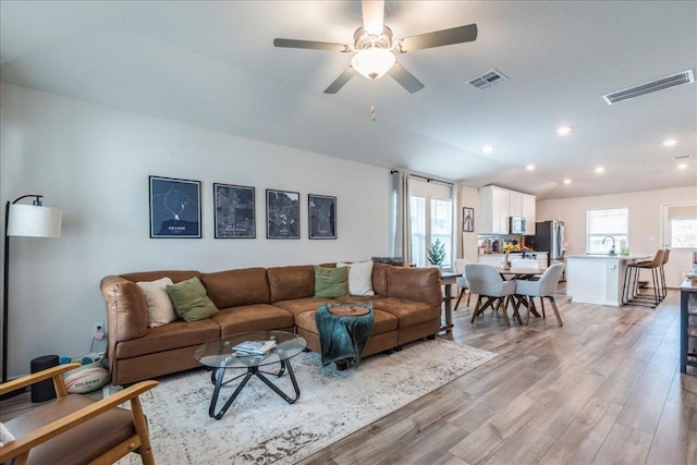 living area with light wood-type flooring, visible vents, vaulted ceiling, and a ceiling fan