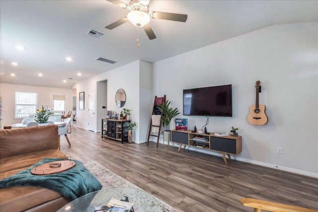 living area with lofted ceiling, visible vents, baseboards, and wood finished floors