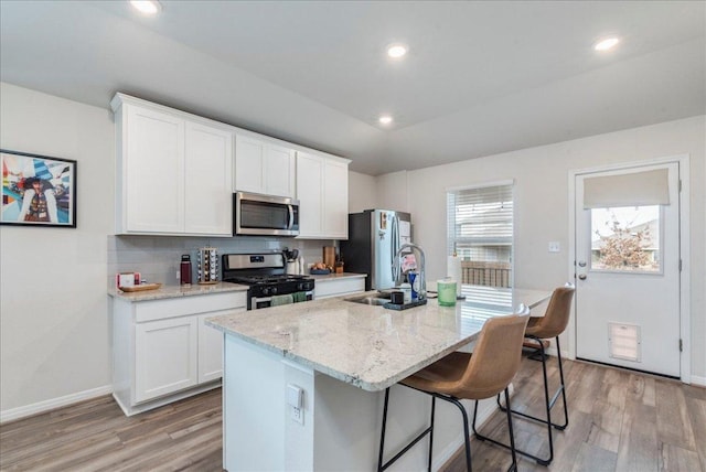 kitchen with an island with sink, light wood-style flooring, appliances with stainless steel finishes, white cabinetry, and a sink