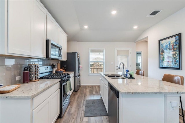 kitchen with tasteful backsplash, visible vents, a kitchen island with sink, stainless steel appliances, and white cabinetry