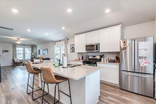 kitchen with white cabinets, light stone counters, appliances with stainless steel finishes, a breakfast bar area, and open floor plan