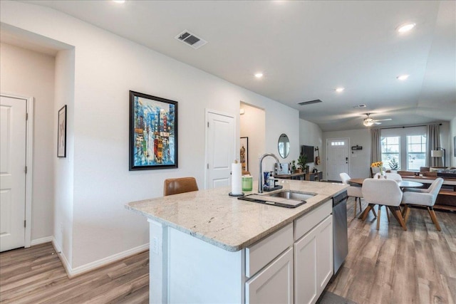 kitchen with stainless steel dishwasher, light wood-style floors, a sink, light stone countertops, and baseboards