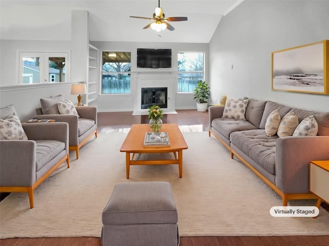 living room featuring a ceiling fan, vaulted ceiling, wood finished floors, and a glass covered fireplace