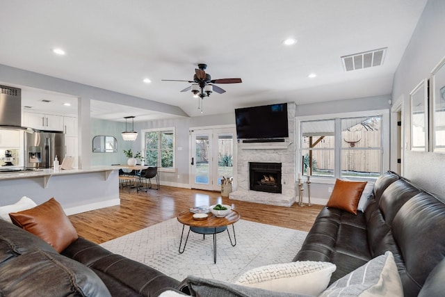 living room featuring recessed lighting, visible vents, a stone fireplace, and light wood finished floors