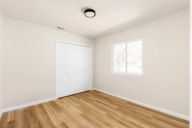 unfurnished bedroom with a closet, visible vents, light wood-style flooring, and baseboards