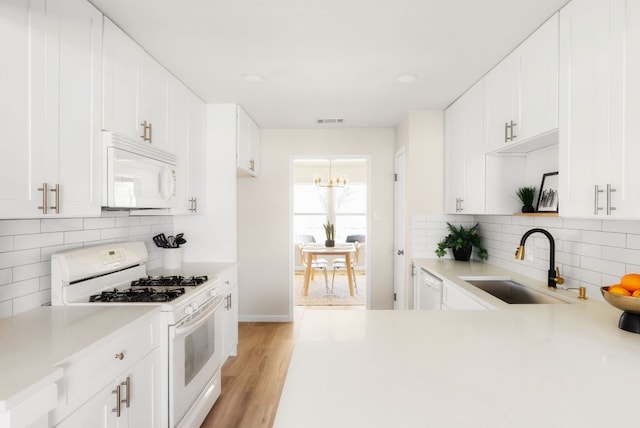 kitchen featuring light wood-style flooring, white appliances, a sink, visible vents, and light countertops