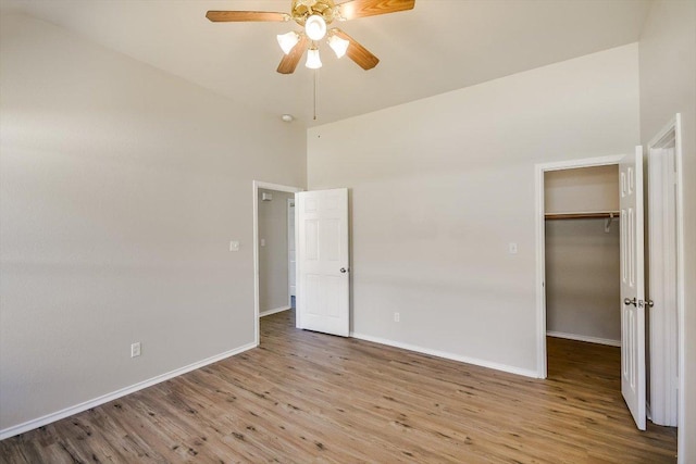 unfurnished bedroom with a walk in closet, a closet, baseboards, and wood finished floors