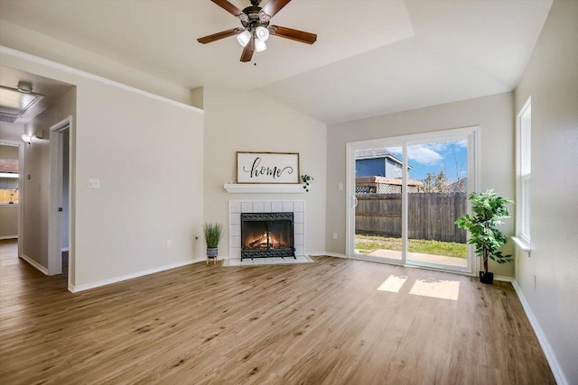 unfurnished living room with a tile fireplace, vaulted ceiling, baseboards, and wood finished floors