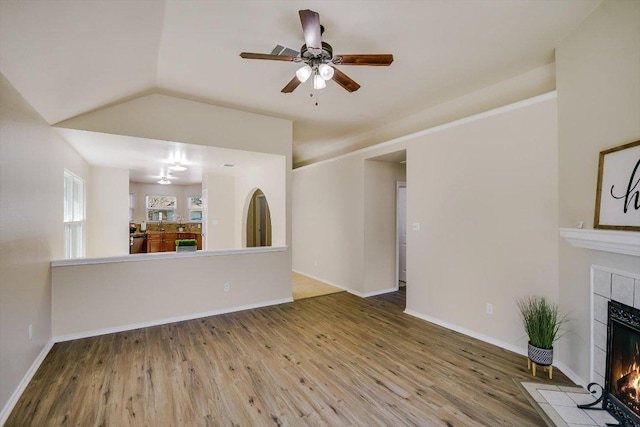 unfurnished living room featuring a tiled fireplace, ceiling fan, vaulted ceiling, wood finished floors, and baseboards