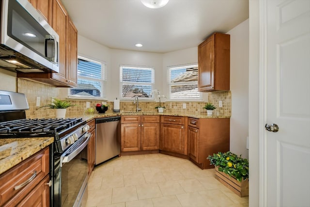 kitchen featuring tasteful backsplash, brown cabinetry, light stone counters, stainless steel appliances, and a sink