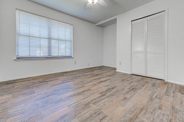 unfurnished bedroom with a closet, ceiling fan, a textured ceiling, wood finished floors, and baseboards