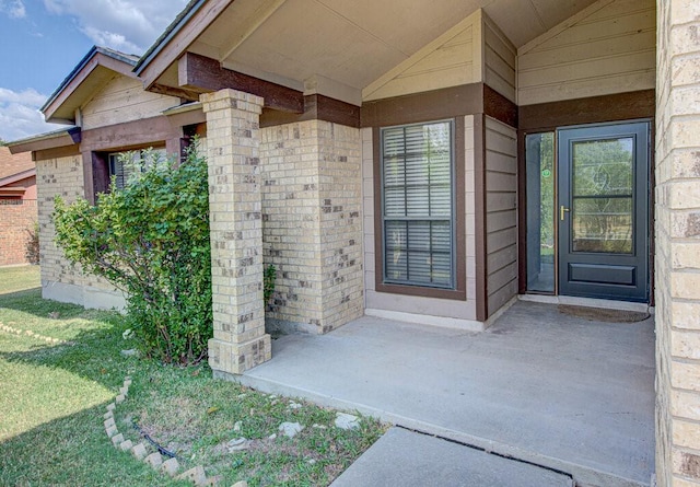 entrance to property featuring brick siding and a lawn