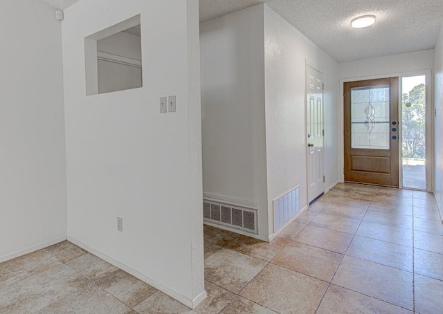 foyer entrance with baseboards, visible vents, a textured ceiling, and light tile patterned flooring