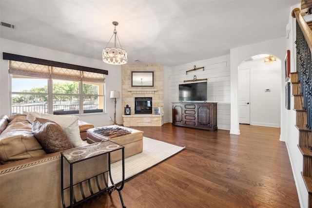 living room featuring arched walkways, a chandelier, a stone fireplace, visible vents, and dark wood-style floors