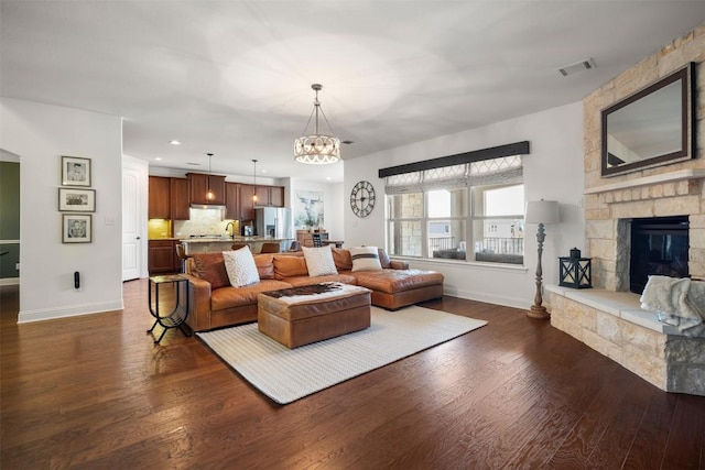 living room featuring baseboards, visible vents, dark wood finished floors, a fireplace, and a notable chandelier