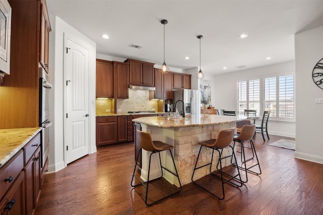 kitchen featuring a breakfast bar, under cabinet range hood, stainless steel appliances, and dark wood-style flooring