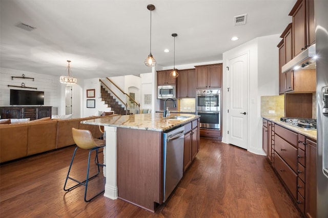 kitchen featuring a breakfast bar area, stainless steel appliances, a sink, visible vents, and open floor plan