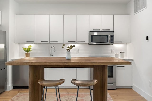 kitchen featuring tasteful backsplash, visible vents, stainless steel microwave, light wood-type flooring, and wooden counters