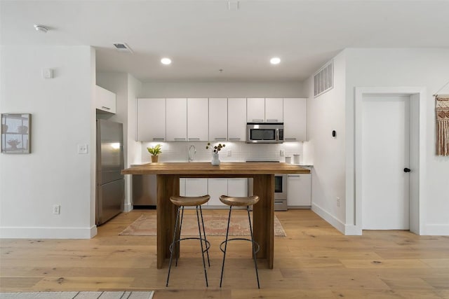 kitchen with white cabinets, butcher block countertops, a kitchen breakfast bar, stainless steel appliances, and backsplash