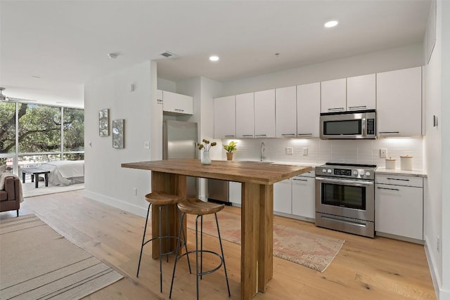 kitchen with stainless steel appliances, butcher block counters, light wood-type flooring, and backsplash