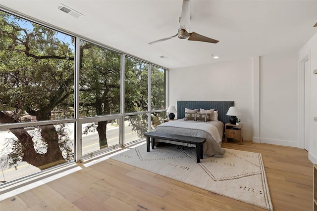 bedroom featuring ceiling fan, visible vents, a wall of windows, and wood finished floors