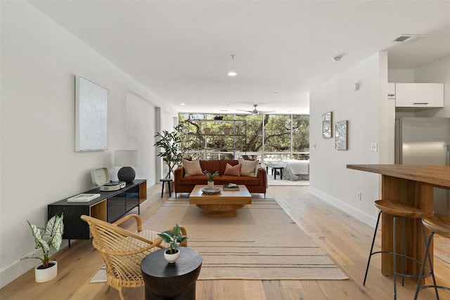 living room with baseboards, visible vents, a wall of windows, light wood-style floors, and recessed lighting