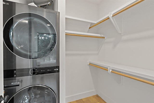 laundry room featuring laundry area, stacked washing maching and dryer, wood finished floors, and baseboards