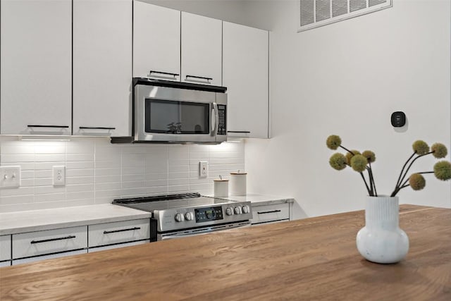 kitchen with visible vents, white cabinetry, appliances with stainless steel finishes, backsplash, and light stone countertops